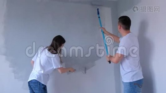 画家们年轻的男女正在用油漆辊画灰色的墙壁。视频