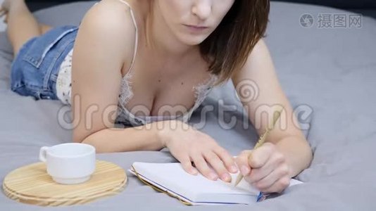 未被认出的白种人女人正在酒店房间的床上用笔记本做笔记。 美丽的女性正在写日记中的符号视频