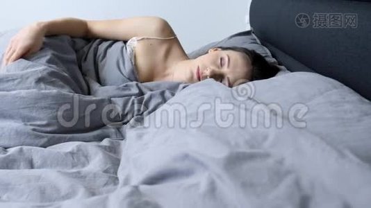 女人一个人在家里的空床上醒来。 年轻的女性独自在酒店房间醒来。 心烦意乱的孤立女孩躺在空床上。 隆隆视频