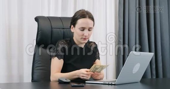 年轻自信的女人在办公室里数美元钞票。 老板娘在办公桌前清点钞票。 女性视频