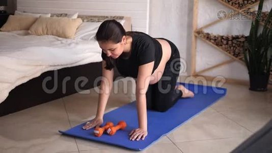 年轻孕妇在家里在蓝色垫子上做健身和瑜伽练习。视频