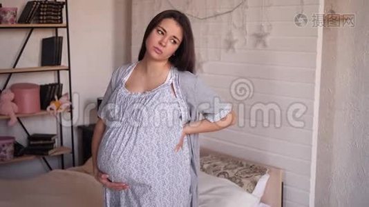 在卧室里有胃痛或背痛的悲伤孕妇穿着睡衣。视频