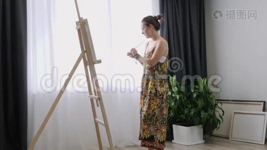 快乐迷人的女人用细刷子在画布上画画。 帆布站在画架上。 艺术家在画架上画画。 女性侧视p视频