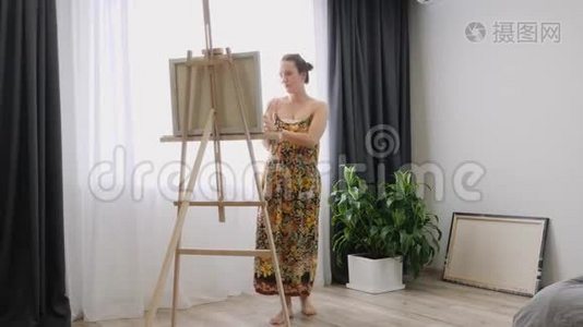 女孩艺术家在艺术工作室，站在画架后面，在画布上画画。 画画油画的年轻女子视频
