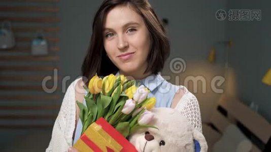 女孩带着礼物，迷人的年轻女子独自在房间里，手里拿着一束黄色郁金香，手里拿着柔软的玩具视频
