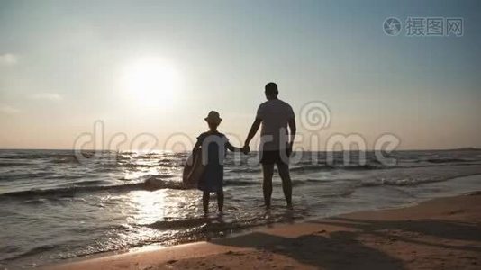 剪影父女在日落时在海滩上玩耍。 友好家庭，旅游，生活方式的概念..视频