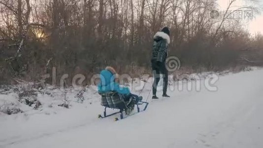 妈妈带着一个孩子坐在雪覆盖的森林上的雪橇上。 开朗的寒假观念..视频