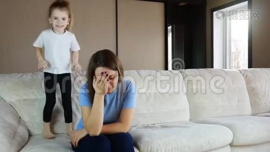 母亲坐在沙发上沉思，活泼的孩子女儿在跳跃玩耍视频