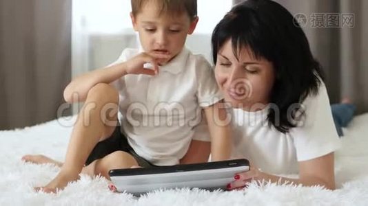 家庭幸福。 母亲和孩子躺在沙发上用平板电脑玩或上网。 协作视频