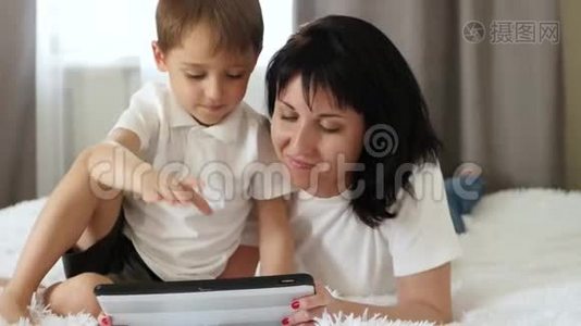 一对母子躺在沙发上用平板电脑上的儿童应用程序看游戏。 幸福的概念视频