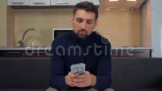 穿着深蓝色套衫和灰色裤子的男人坐在沙发上，拿着一包钱，竖起大拇指视频