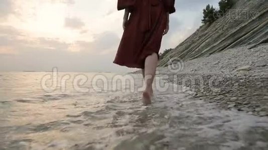 近景后景的双腿白种人女孩走在海边的石头海岸的水中，走向夕阳。视频