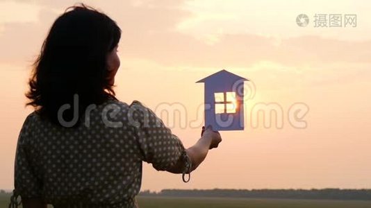 日落时剪影纸房。 女孩养了一个纸房子，梦想着一个舒适的大房子和一个幸福的家庭。视频