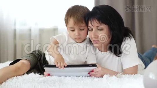 母子俩在平板电脑上看电影，躺在沙发上.. 幸福家庭、养育子女、工作的概念视频