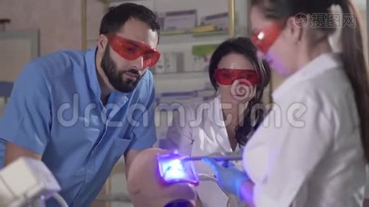 三名专业牙科助理使用人体模型上的固化灯。 中东男子和高加索妇女视频