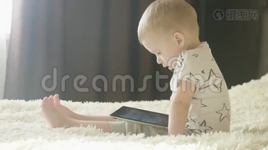 小男孩坐在床上，在房间里的平板电脑上玩。 育和技术理念..视频