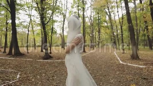 美丽可爱的新娘穿着婚纱在公园里奔跑。 慢动作视频