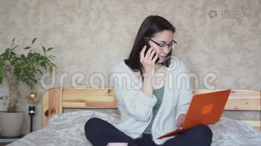 一个年轻迷人的女孩正在用手机和电脑上的数据进行比较。视频