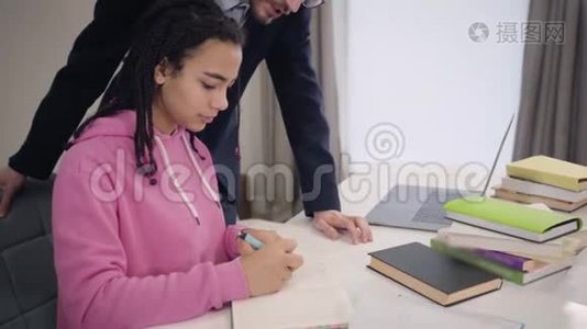 穿着悲伤的非裔美国女孩坐在桌子旁，她的白人家庭教师站在桌子旁说话视频