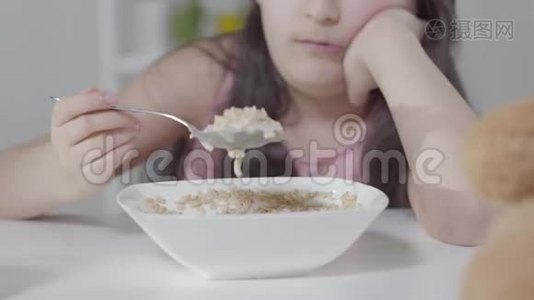 无聊得认不出来的小女孩用勺子拌麦片。不快乐的中东孩子早上吃早餐视频