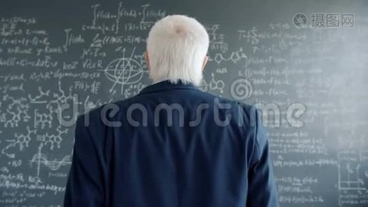 穿西装的成熟男人走向黑板墙，用公式看方程式视频