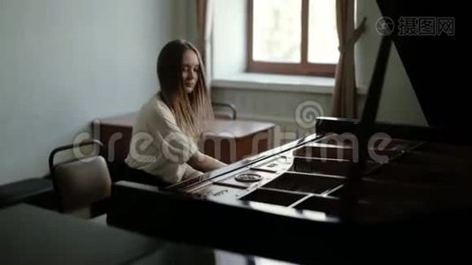 一位年轻的钢琴家，长发在窗户附近的大钢琴上弹奏音乐视频