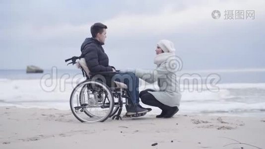 年轻的女人坐在轮椅上的男孩面前，说话。 母亲或支持无效投标视频