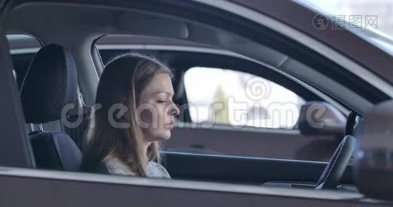 年轻自信的高加索女人坐在汽车里，摸着方向盘。 女士选择汽车视频