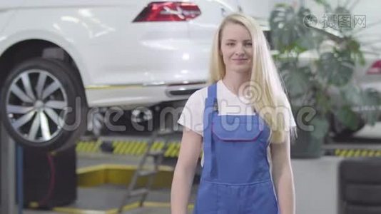 中镜头的年轻白种人女人交叉双手和微笑。 金发女汽车修理工在工作场所摆姿势视频