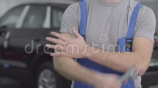 不可辨认的白种人穿着蓝色工作袍，在黑色汽车的背景下用扳手交叉双手。 男性视频