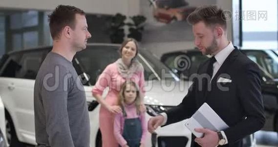 快乐的白种人母女在他们的丈夫和父亲拿着车钥匙的背景下做胜利的手势视频
