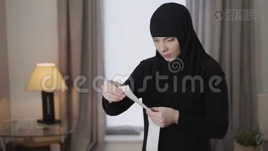 成年穆斯林女士穿着传统服装看着大收据的肖像，表情震惊。 东部青年视频