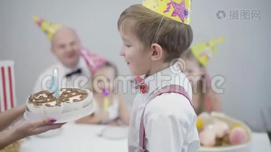 小白种人男孩在生日蛋糕上吹灭了图四上的蜡烛。 派对帽庆祝的年轻人视频