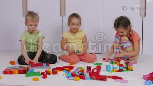 孩子们坐在游戏室的地毯上，玩建造者乐高积木视频
