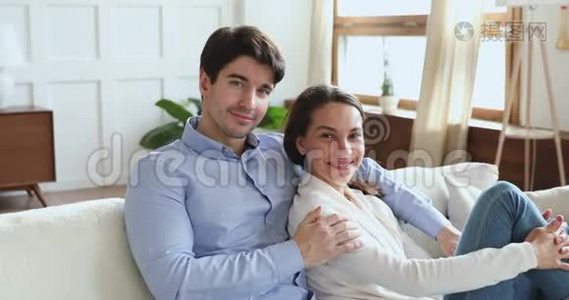 微笑的年轻夫妇坐在沙发上看着摄像机视频