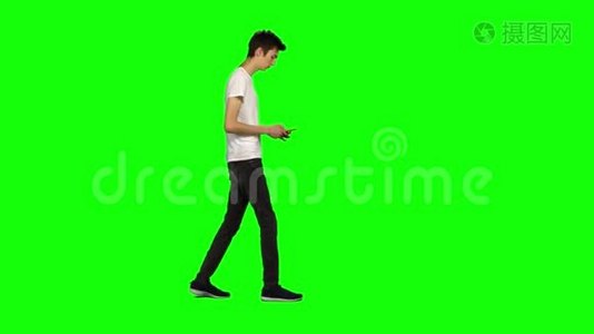 高个子瘦小的年轻人平静地走着，在绿色屏幕上发短信给他的手机。 铬钥匙。 侧写视图。视频