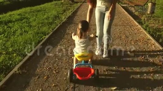 妈妈教女儿在公园里骑自行车。 幼儿学习骑自行车.. 妈妈玩她的小东西视频