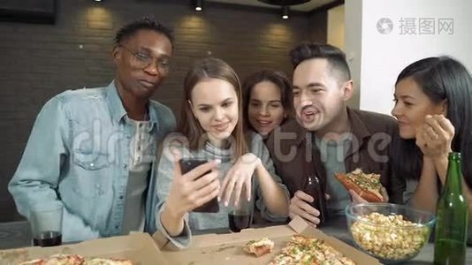 多民族的朋友看着智能手机，在酒吧或家里谈笑风生，吃披萨和零食视频