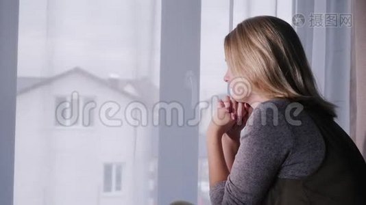 一个悲伤的女人坐在窗台上，望着窗外的房子视频