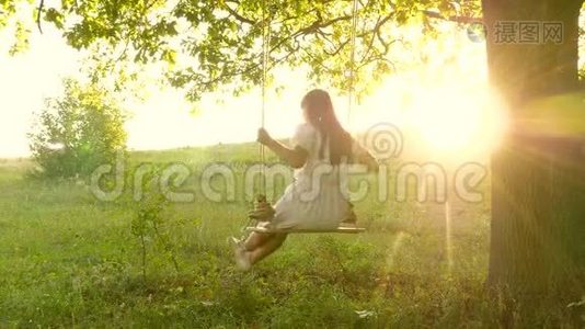 年轻女孩在阳光下在橡树枝上荡秋千。 飞行的梦想。 快乐的童年概念。 一个漂亮的女孩视频
