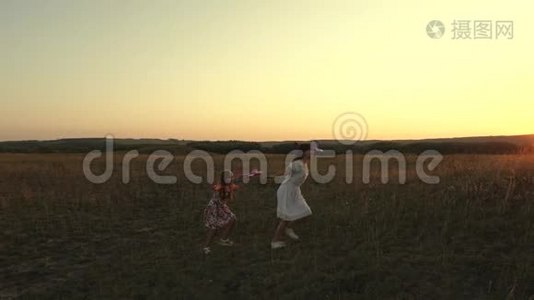 梦想飞翔。快乐童年理念。两个女孩在日落时玩玩具飞机。太阳背景下的孩子们视频