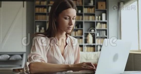 年轻的成年商务女性在笔记本电脑上打字，坐在桌子上视频