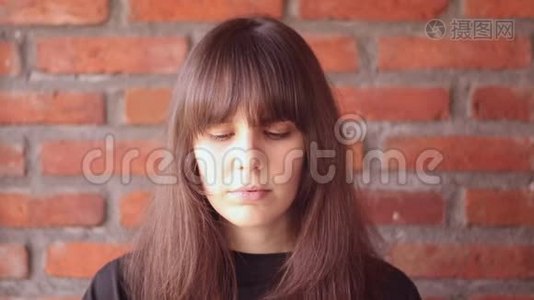 年轻的非常沮丧的黑发女人带着刘海，穿着一件黑色T恤，在砖墙背景上感到羞愧视频
