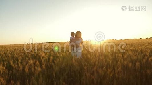 一个快乐的妈妈在日落时带着一个小女儿在一片麦田里抱着她。 宝贝和她妈妈一起走过视频