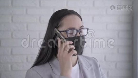 一个戴着黑色医疗面具的年轻女人在电话里说话。 冠状病毒大流行视频