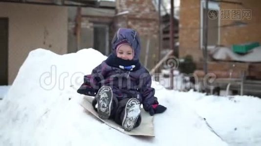 一个孩子在雪地滑梯上翻滚。 冬天在街上玩。 在寒冷的冬天，孩子穿着一件夹克和一件视频