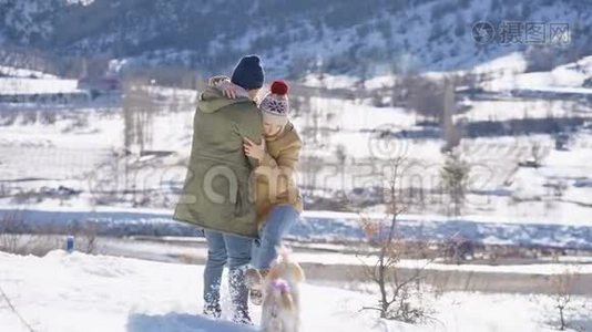 一对年轻漂亮的夫妇在一个阳光明媚的日子里和一只活泼的小狗在雪山上玩。 寒假概念。视频