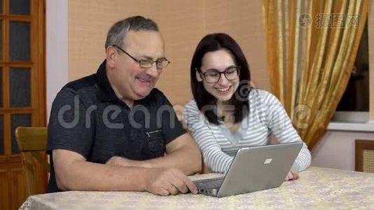 一个女儿和她父亲通过笔记本电脑通过视频交流与朋友交流。 一个年轻的女人和一个老的视频
