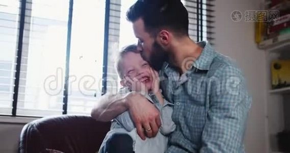 快乐的年轻白种人父亲接吻的肖像，在现代轻屋慢动作中与可爱的微笑的小儿子玩耍。视频