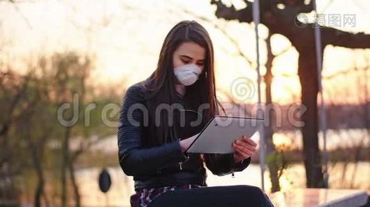 日落时分，一位带着平板电脑的女士集中在公园工作，她戴着一个防护面罩来保护和安全视频